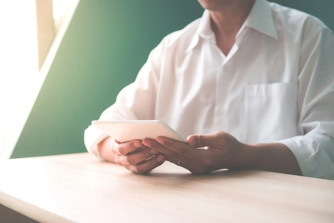 Крупный план счастливого улыбающегося бизнесмена или работодателя, работающего с цифровым планшетом и разговаривающего по смартфону в современном офисном интерьере, со световыми бликами; снимок в стиле винтажного эффекта.